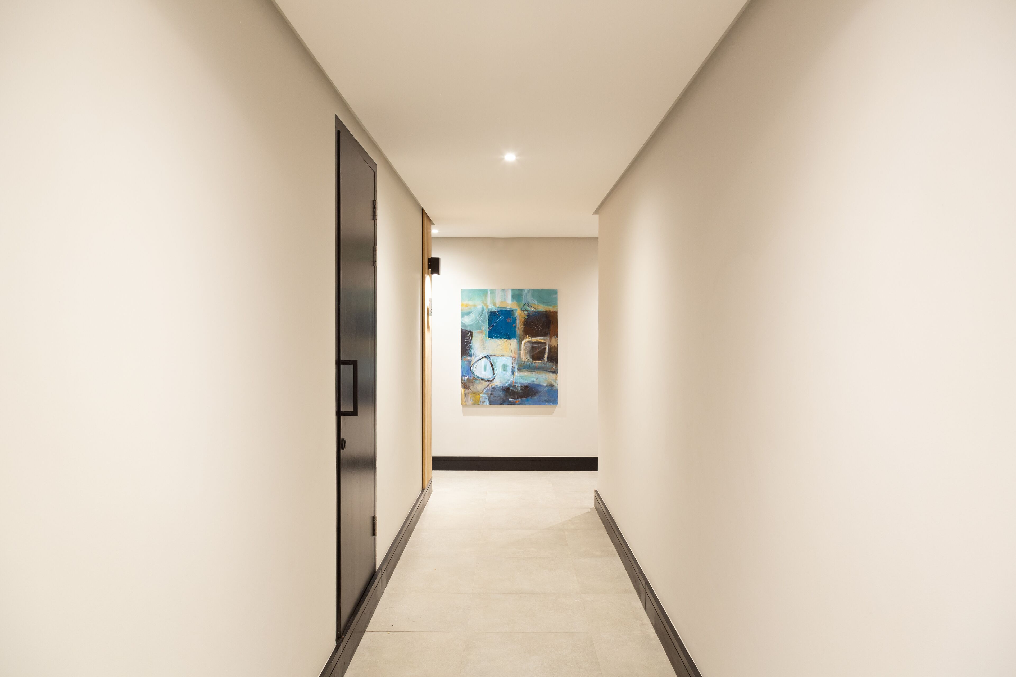 A hallway with a modern design, featuring a large abstract painting on the wall and a door on the left.