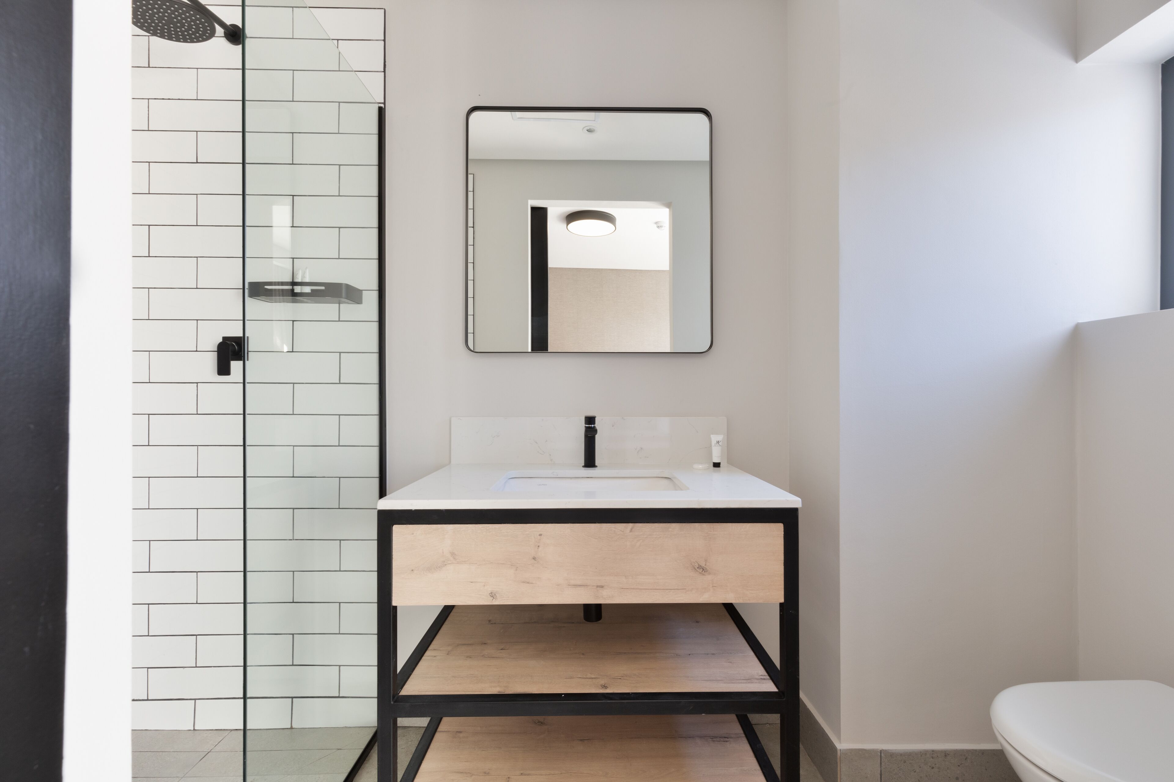 A modern bathroom with a white tiled shower, a wooden vanity with a sink, and a toilet.