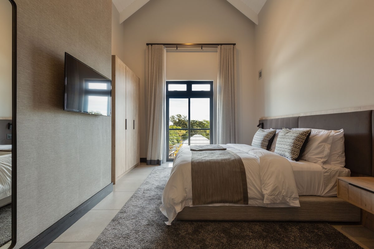 Un dormitorio moderno con una cama grande, un televisor de pantalla plana y vistas a la vegetación a través de una ventana.