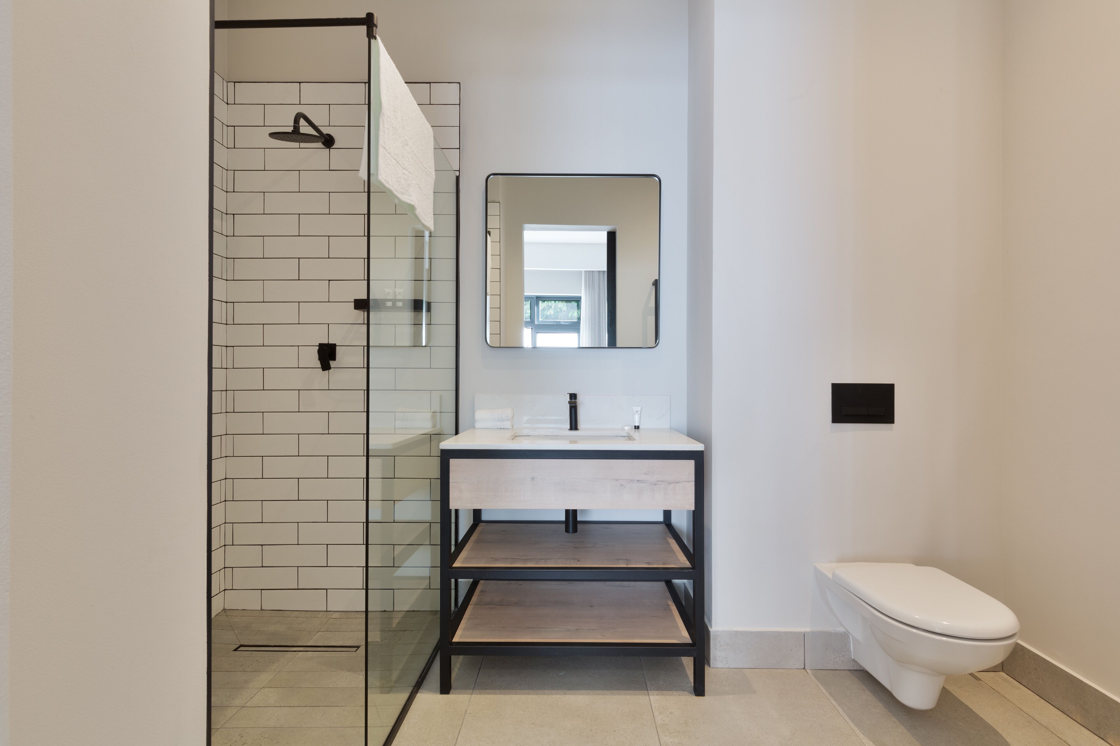 Un baño moderno con cabina de ducha de vidrio, un lavamanos blanco con un espejo encima y un inodoro blanco.