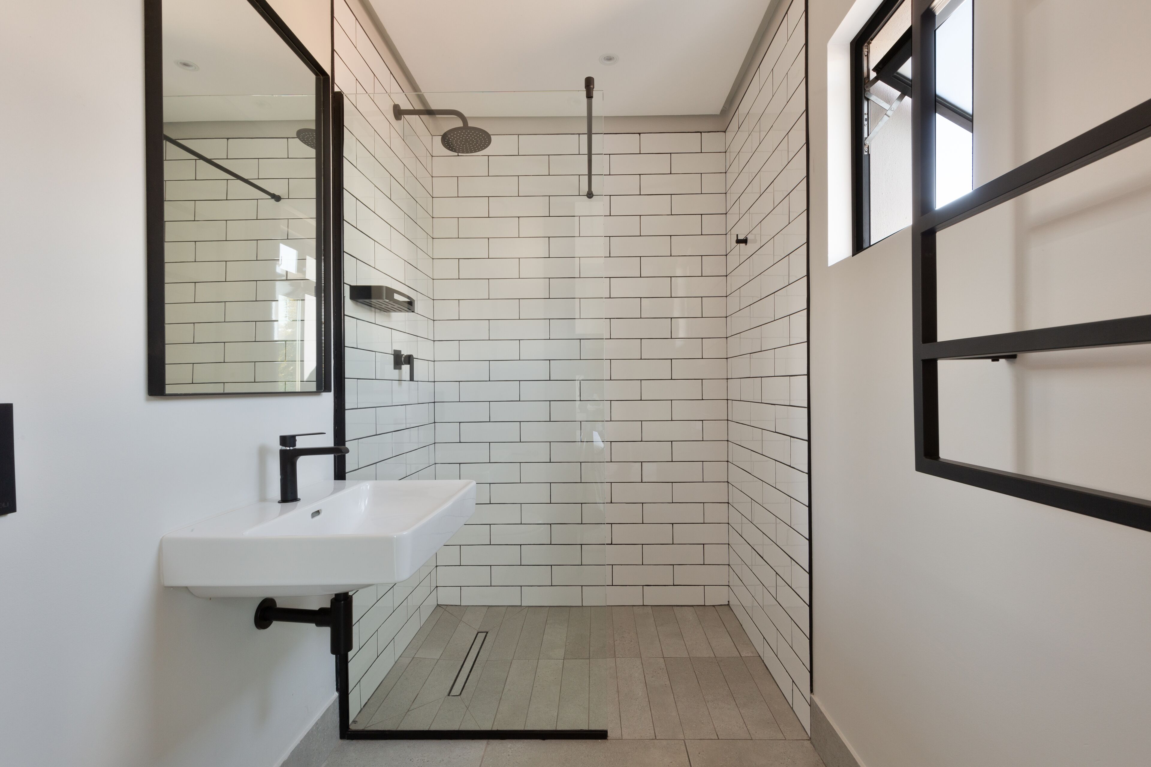 A modern bathroom with white subway tiles, a white sink, a black faucet, and a shower with a black frame.