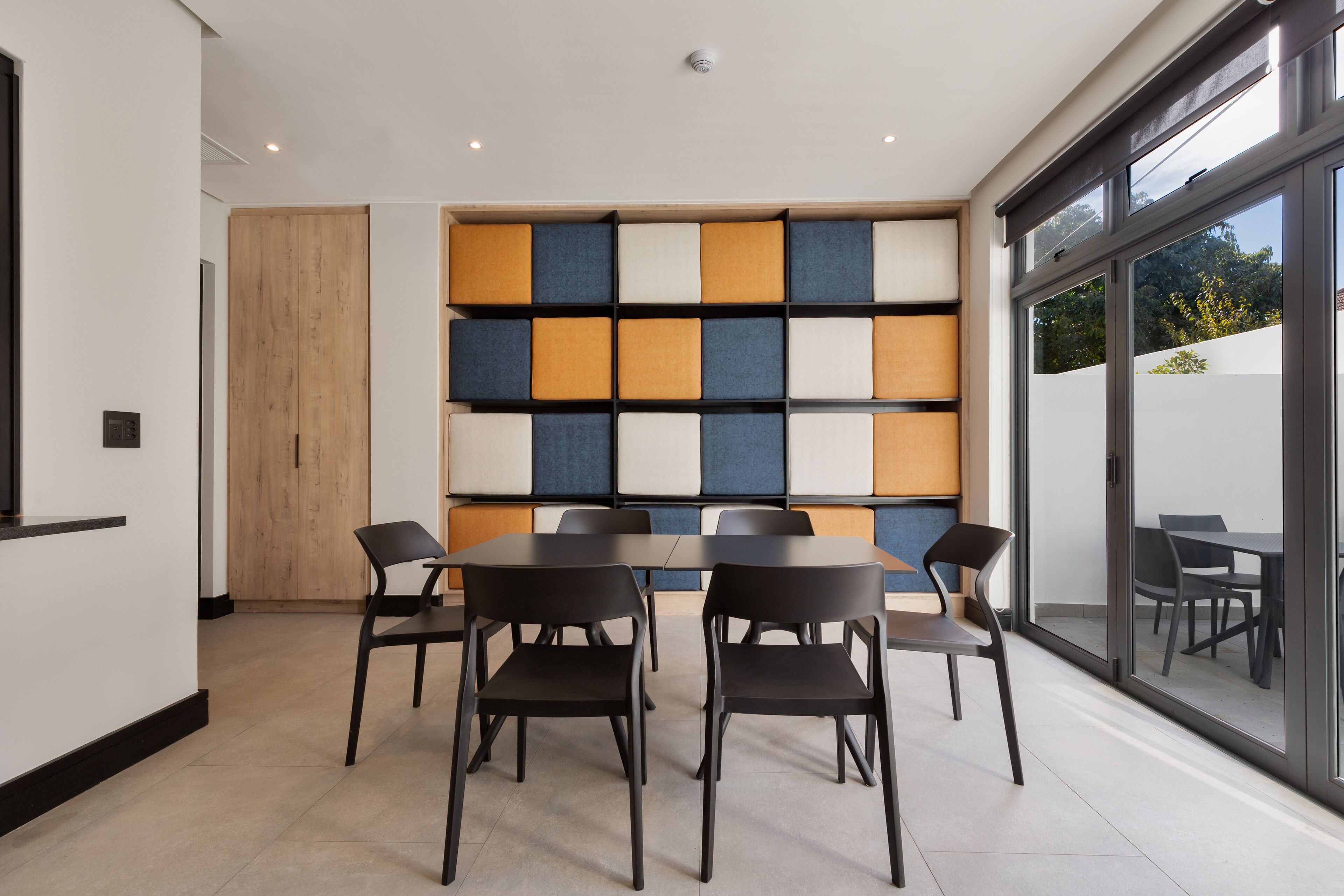 Una sala de reuniones moderna con un muro de vidrio, una puerta de madera y un panel de pared colorido.
