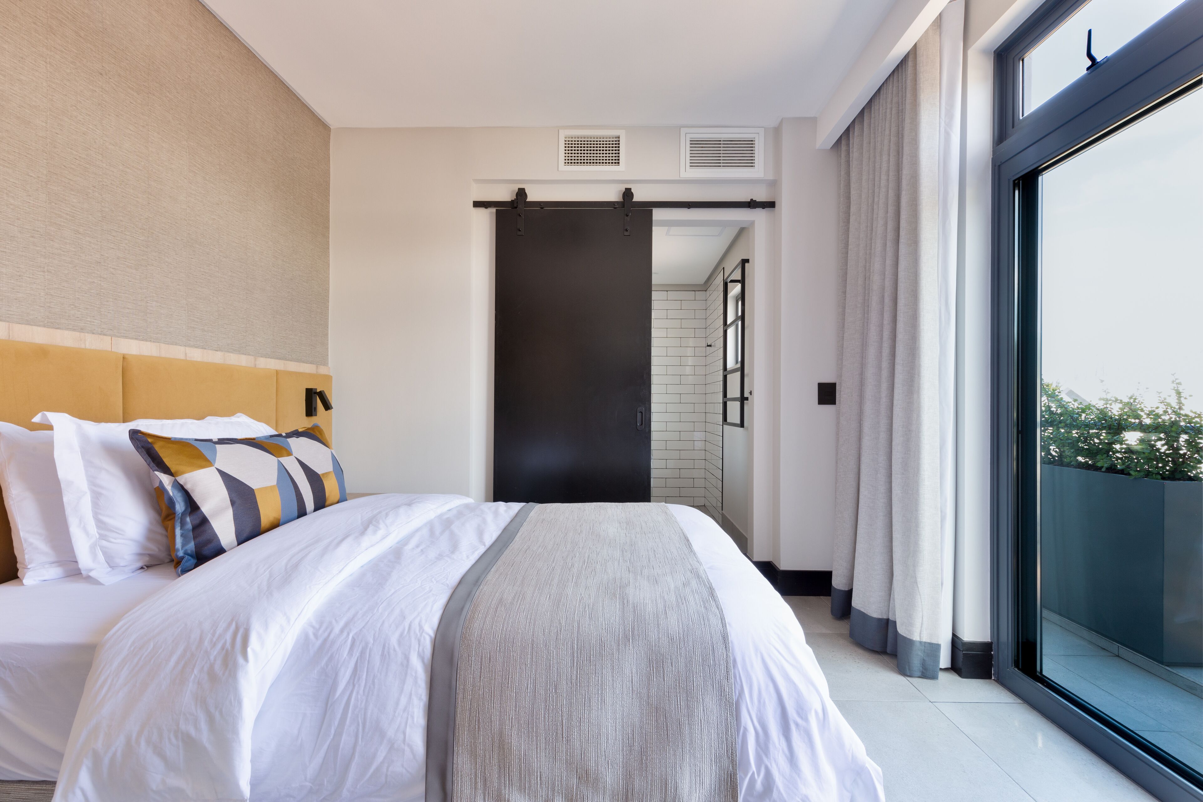 Quarto de hotel moderno com uma cama grande, porta deslizante para uma varanda e vista para o exterior.