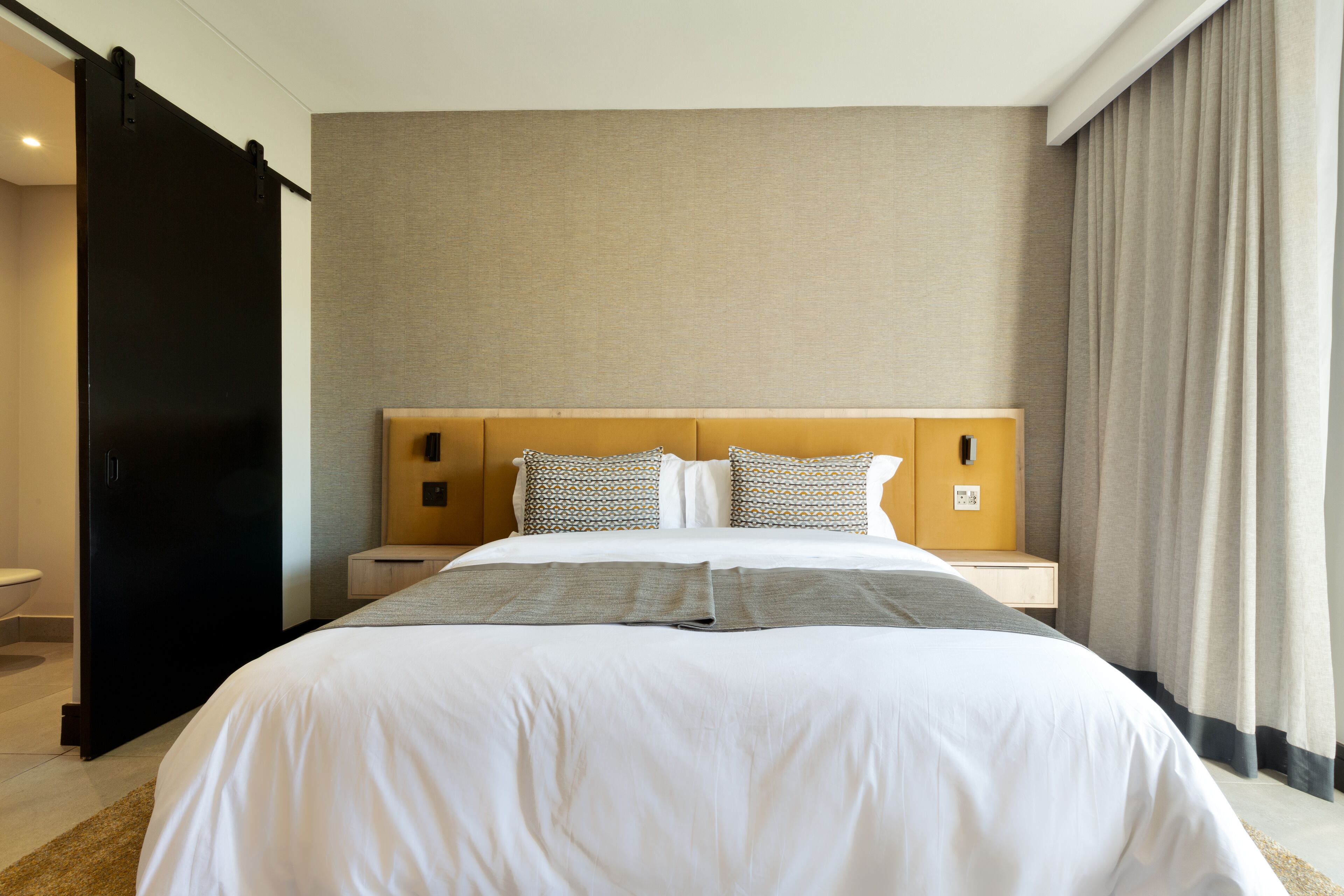 Una habitación de hotel con una cama grande, cabecera de madera y una decoración en tonos neutros.