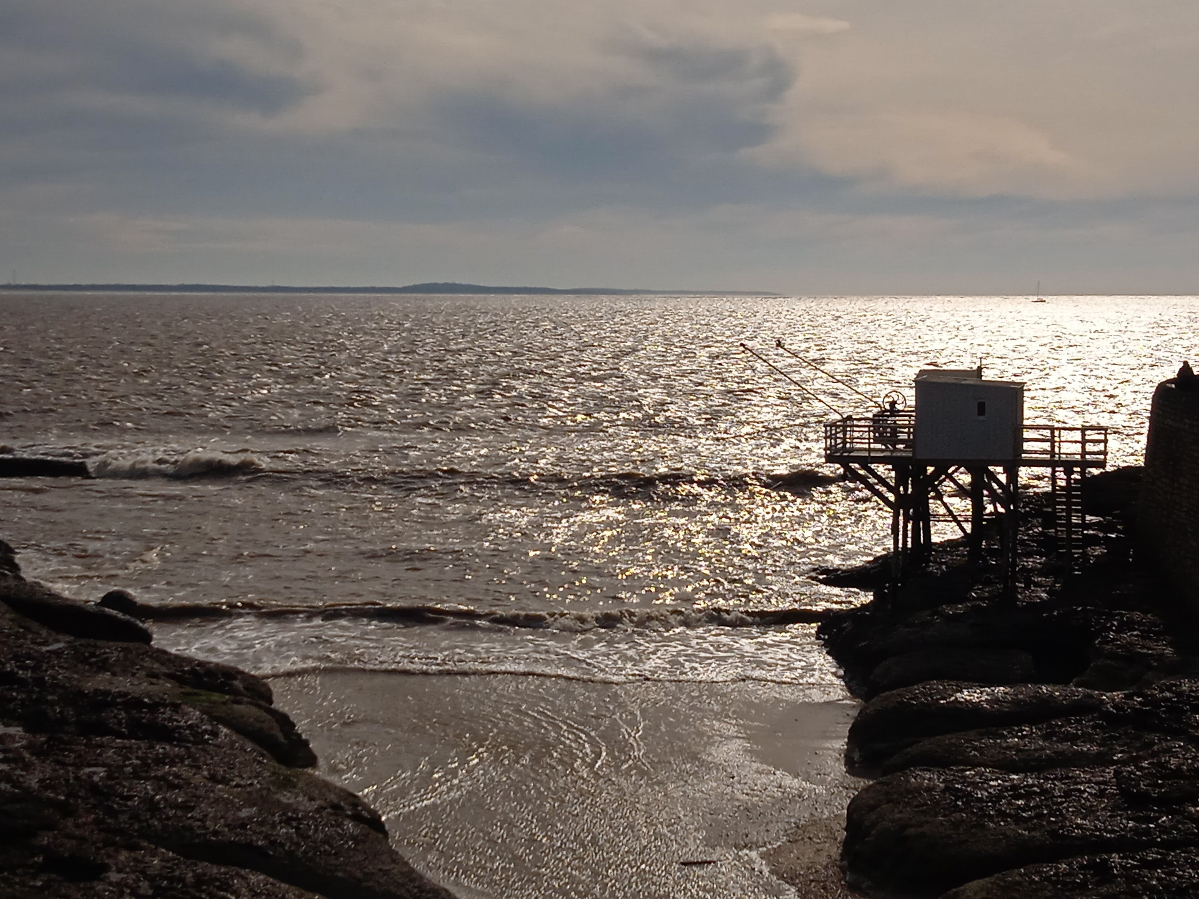 A coastal scene with a rocky shoreline, a small structure on stilts, and the ocean in the background.