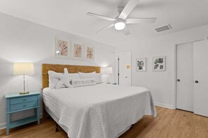 A bedroom with a bed, nightstand, wall art, ceiling fan, and a door.