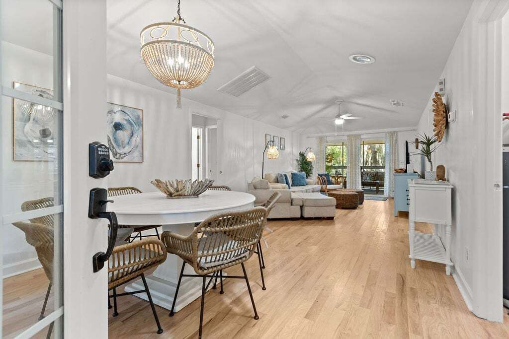 A spacious living area with a round dining table, wicker chairs, a sofa, and a chandelier.