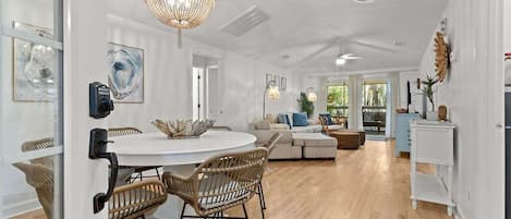 A spacious living area with a round dining table, wicker chairs, a sofa, and a chandelier.