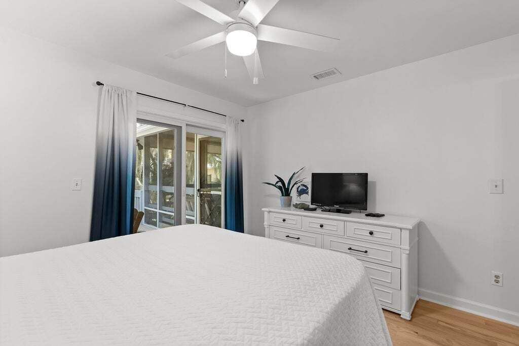 Un dormitorio con cama, televisor sobre una cómoda y ventilador de techo.