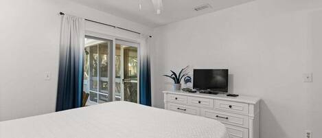 Un dormitorio con cama, televisor sobre una cómoda y ventilador de techo.
