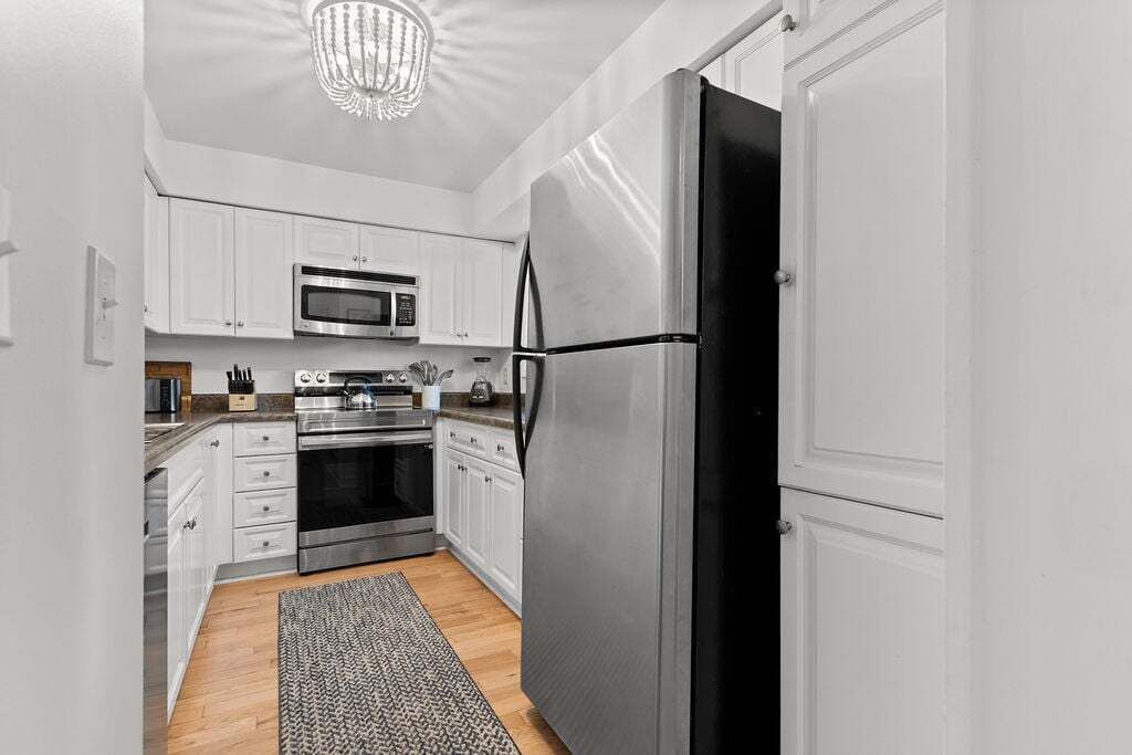 A modern kitchen with white cabinetry, stainless steel appliances, and a patterned rug.