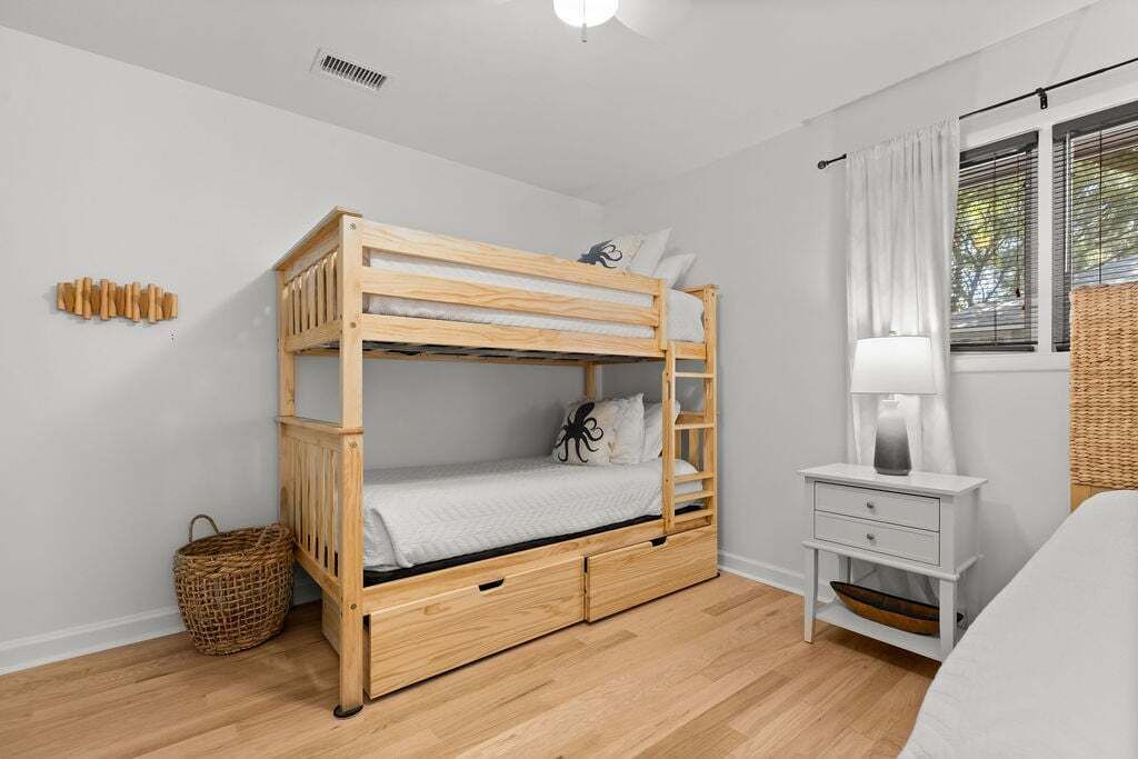 Un letto a castello con una scala, un comodino con cassetti, una lampada e un cesto in vimini.