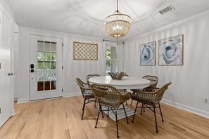 A dining room with a round table, six wicker chairs, a chandelier, and abstract wall art.