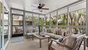 A sunlit room with a ceiling fan, a sofa, a coffee table, and a view of trees through large windows. - 3 BD/2 BA  Pet Friendly Summerwind! Amenity Access included! Close to Beaches, Pools, Dining & Golf! (Seabrook Island)