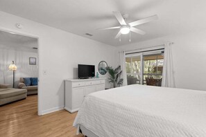Een slaapkamer met een bed, een televisie op een dressoir, een plafondventilator en uitzicht door een raam.