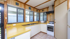 A compact kitchen with wooden paneling, a yellow countertop, a sink, a stove, and a window with blinds.