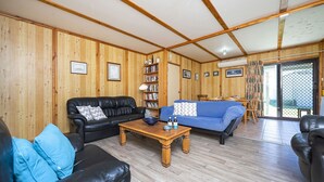 A cozy living room with wooden walls, a black leather sofa, a blue sofa, and a wooden coffee table.