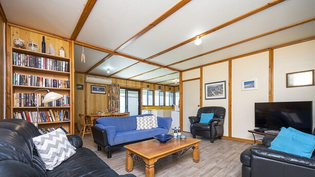 A living room with a wooden bookshelf, a blue sofa, a black leather sofa, a wooden coffee table, and a television.