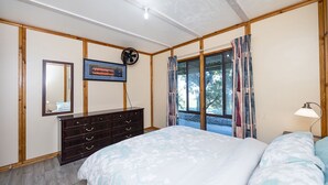 A bedroom with a bed, a dresser, a mirror, a fan, and a window with curtains.