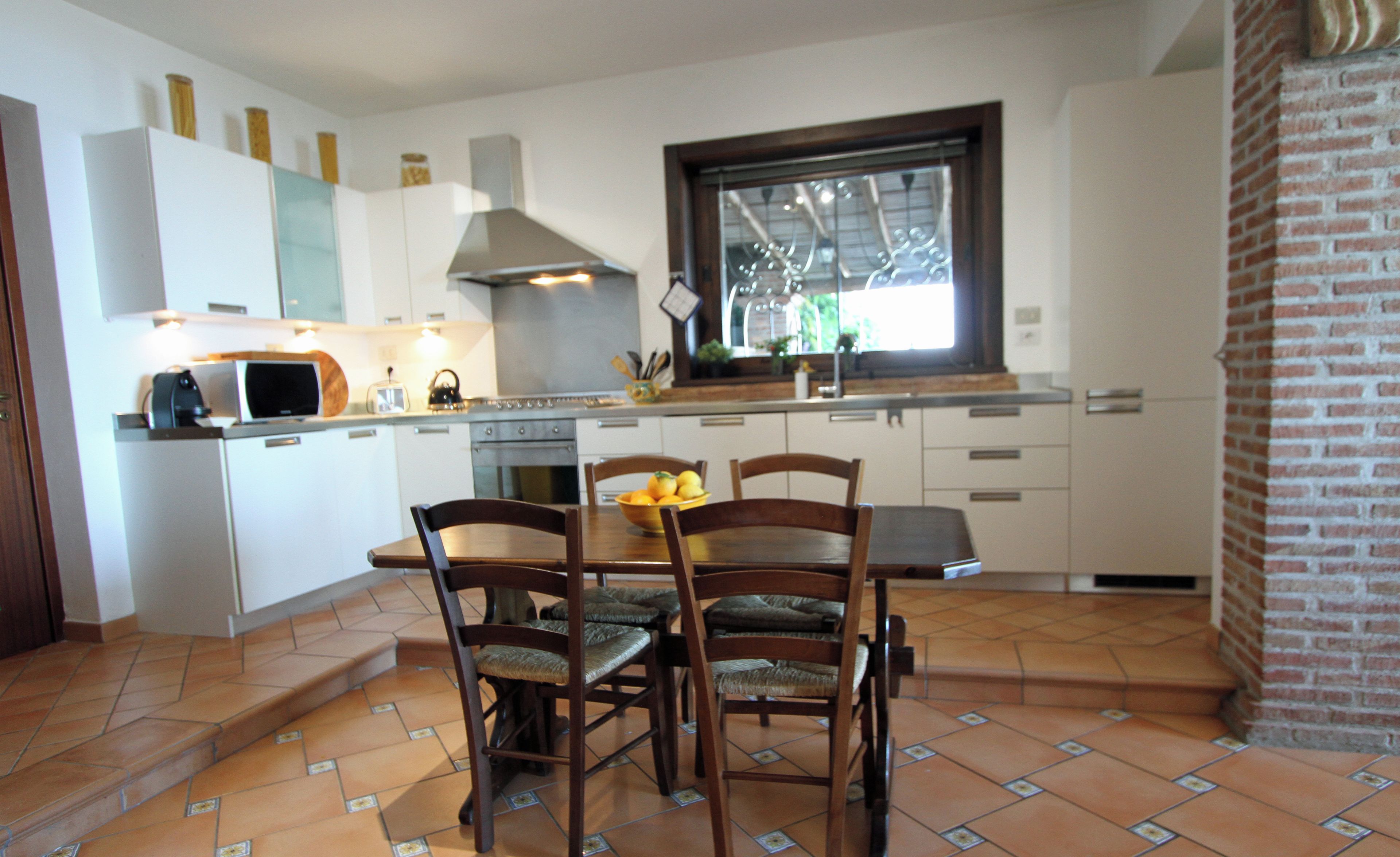 Una cucina con mobili bianchi, un piano cottura e un'area pranzo con sedie e tavolo in legno.