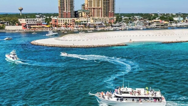 Zona costera con un barco grande, una playa arenosa y un complejo hotelero al fondo.