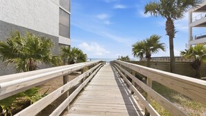 Un paseo marítimo de madera que conduce a un edificio de fachada blanca y palmeras.