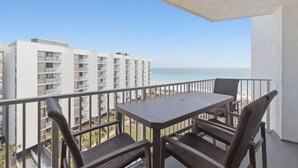 Un balcón con mesa y sillas, con vista a una playa y un edificio blanco.