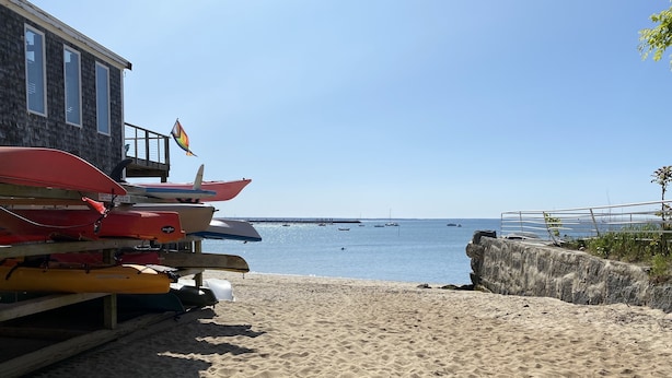 Una playa arenosa con kayaks apilados sobre una plataforma de madera.