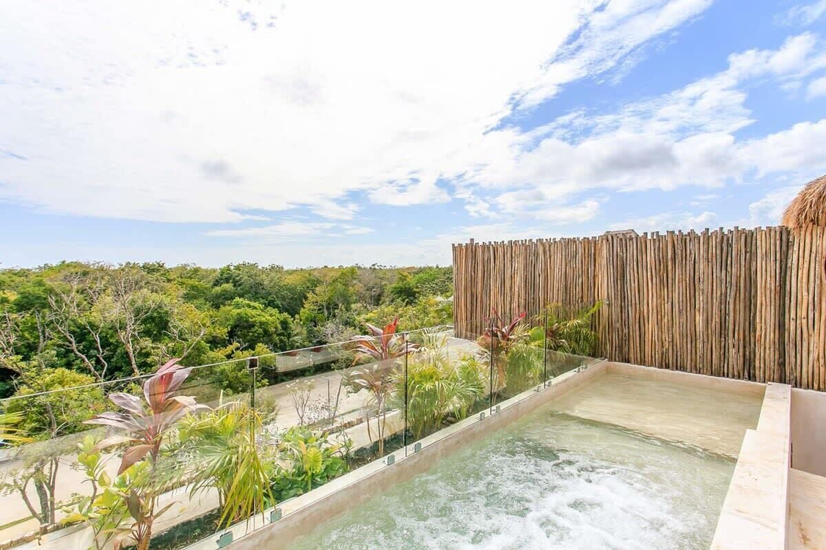 A rooftop pool with a wooden fence and lush greenery in the background.