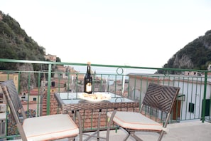 A balcony with a table set for two, a bottle of wine, and a plate of food.