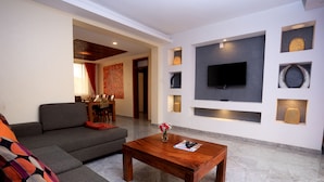 A modern living room with a grey sofa, a wooden coffee table, and a flat-screen TV mounted on the wall. - Deluxe 3-bed Apartment With Swimming Pool (Kampala)