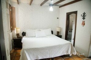 Quarto com cama, duas mesinhas de cabeceira, luminária na parede e porta decorada com uma coruja.