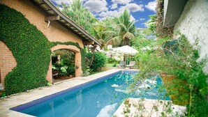 A swimming pool surrounded by lush greenery and a brick wall.