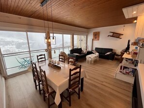 Un vaste espace de vie doté d’un plafond en bois, d’une table à manger avec des chaises, d’un canapé et d’une petite table blanche.