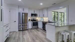 A modern kitchen with white cabinetry, stainless steel appliances, and a large window providing natural light. - Beautiful renovated home in the heart of Sea Pines with Private Pool! (Hilton Head Island)