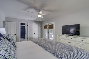Una camera da letto con un letto, una televisione, un ventilatore a soffitto e una porta che conduce al bagno.