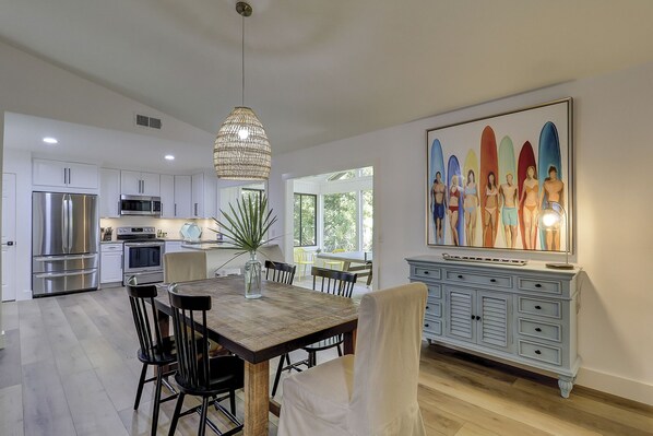 Una cucina moderna con elettrodomestici in acciaio inossidabile, un'area pranzo con tavolo e sedie in legno e un grande quadro appeso al muro.