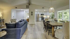 A modern kitchen with stainless steel appliances, a dining area with a wooden table and chairs, and a living room with a blue sofa and a lamp. - Beautiful renovated home in the heart of Sea Pines with Private Pool! (Hilton Head Island)