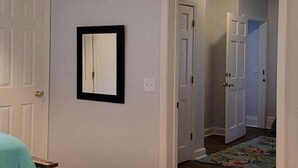 A hallway with white doors, a framed mirror on the wall, and a floral-patterned rug on the floor. - 25b Olive Ave.- North Rehoboth Cottage with prime ocean-block location (Rehoboth Beach)