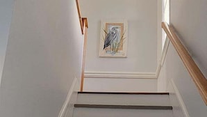 A staircase with wooden handrails and a framed artwork of a bird on the wall. - 25b Olive Ave.- North Rehoboth Cottage with prime ocean-block location (Rehoboth Beach)