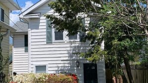A two-story house with a front door, a small porch, and a garden with various plants and flowers. - 25b Olive Ave.- North Rehoboth Cottage with prime ocean-block location (Rehoboth Beach)