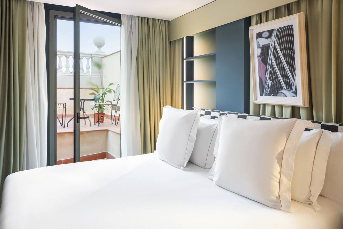 A hotel room with a large bed, a balcony with a table and chairs, and a framed picture on the wall.