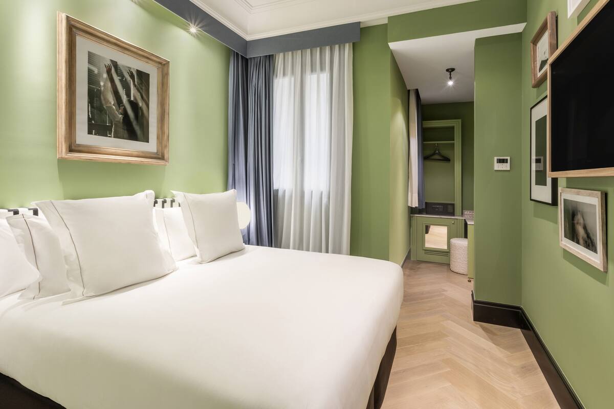 A hotel room with a large bed, a mirror, a wardrobe, and a bathroom visible through an open door.