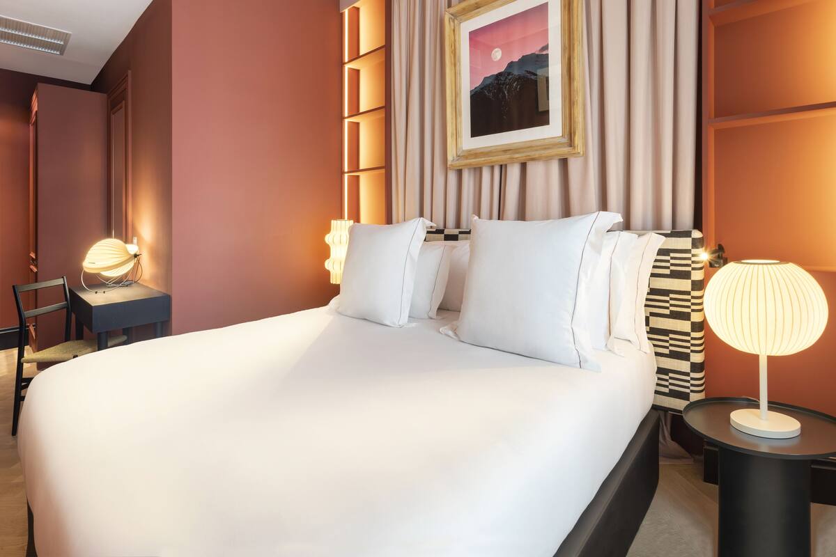A hotel room with a large bed, two bedside tables with lamps, a chair, and a framed picture on the wall.