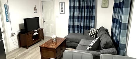A living room with a sofa, a coffee table, a TV on a wooden cabinet, and a door.