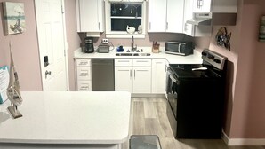 A compact kitchen with white cabinets, a dishwasher, a microwave, a stove, and a sink. - Beachy Paradise (Indian Rocks Beach)