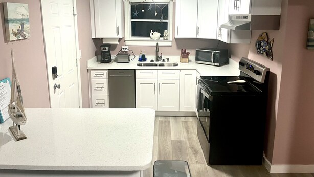 Una cocina compacta con armarios blancos, lavavajillas, microondas, estufa y fregadero.
