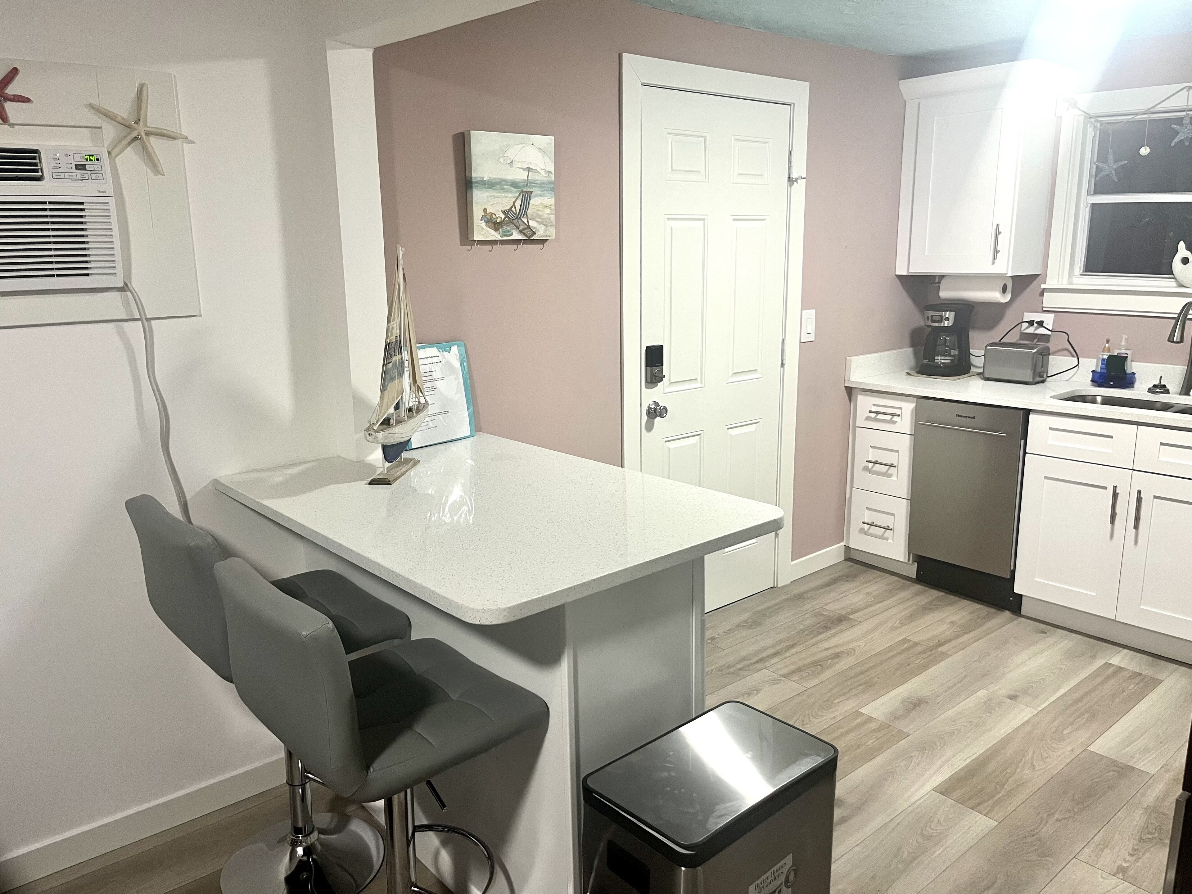 A modern kitchen with white cabinets, a built-in dishwasher, and a coffee maker.