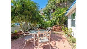 A patio with a round table and chairs, surrounded by lush greenery and a white picket fence. - Beachy Paradise (Indian Rocks Beach)