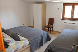 A bedroom with two beds, a wardrobe, a chair, and a radiator.
